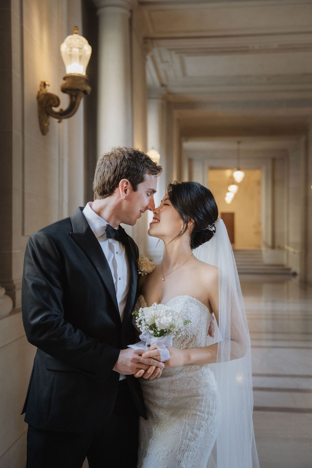 An intimate wedding moment captured in a historic hallway with classical lighting fixtures.