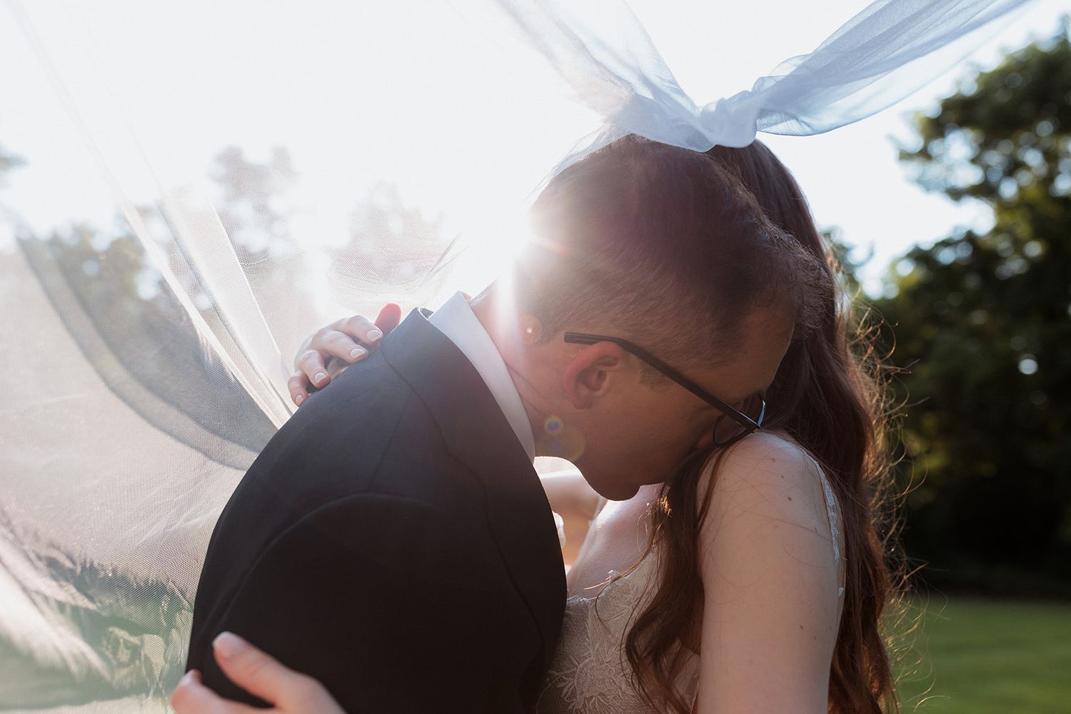 Romantic sunset kiss between couple with veil flowing in the breeze.