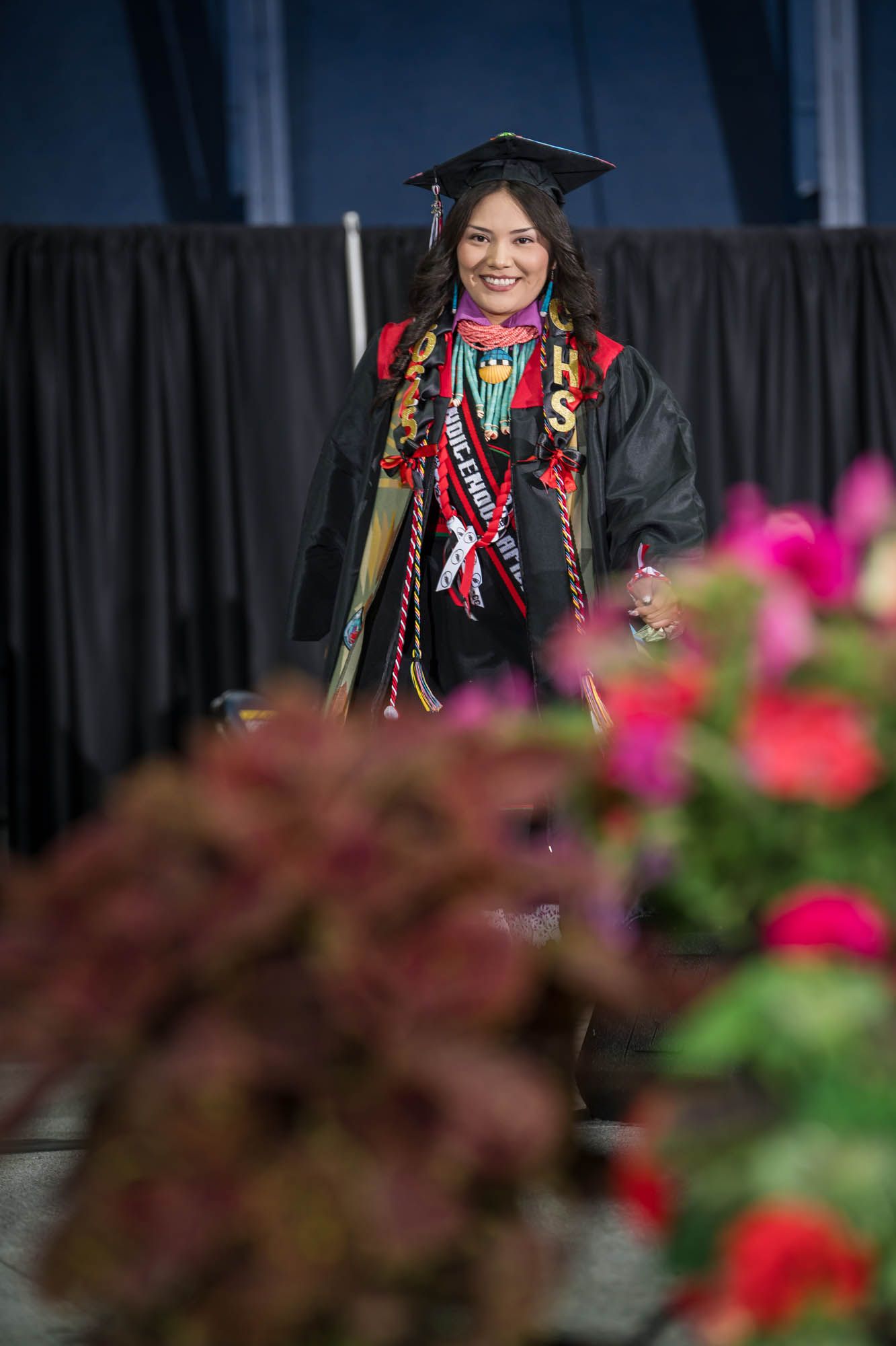 Luvelle Lomahoyourna, standing at a podium, welcomed the 2025 CHS Graduation crowd in Hopi.