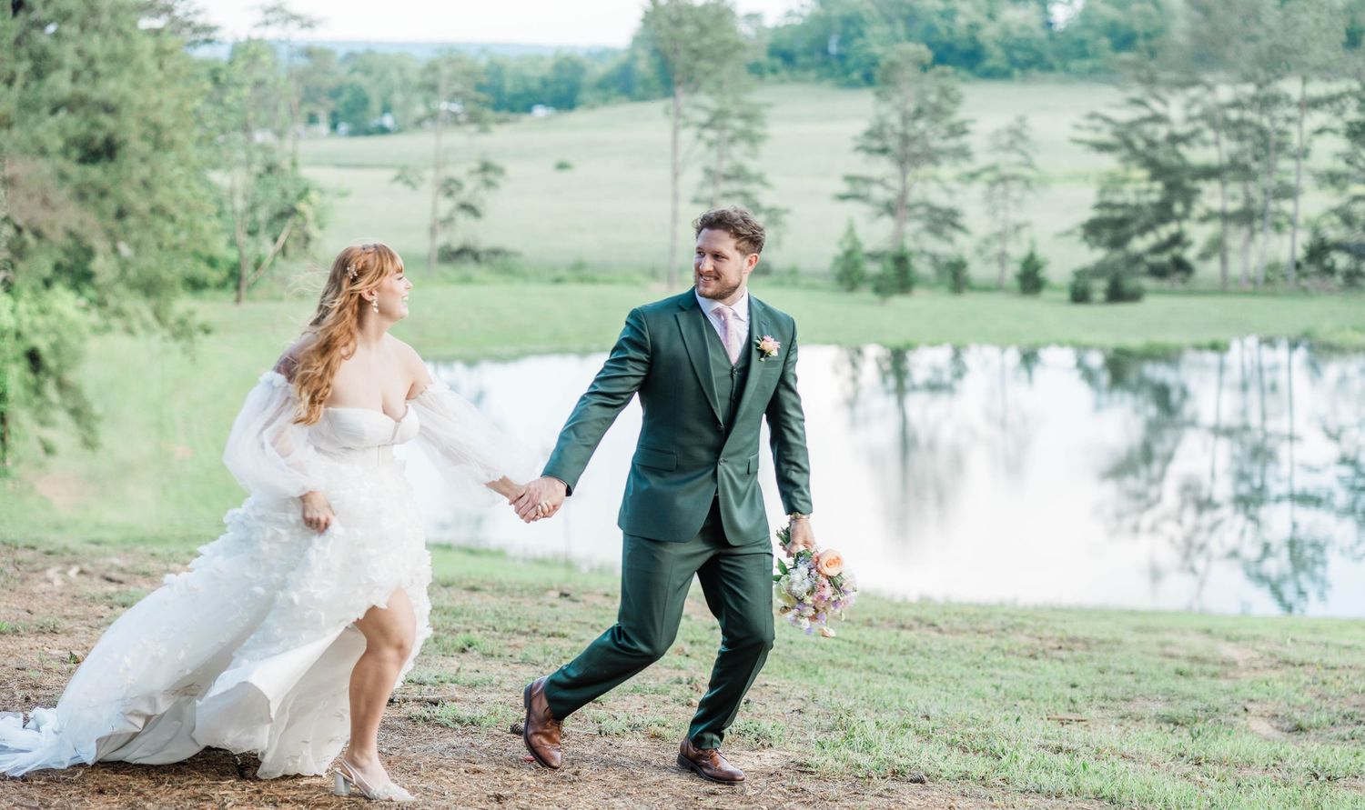 Bride and groom running together on grassy hill with waterfall in background.