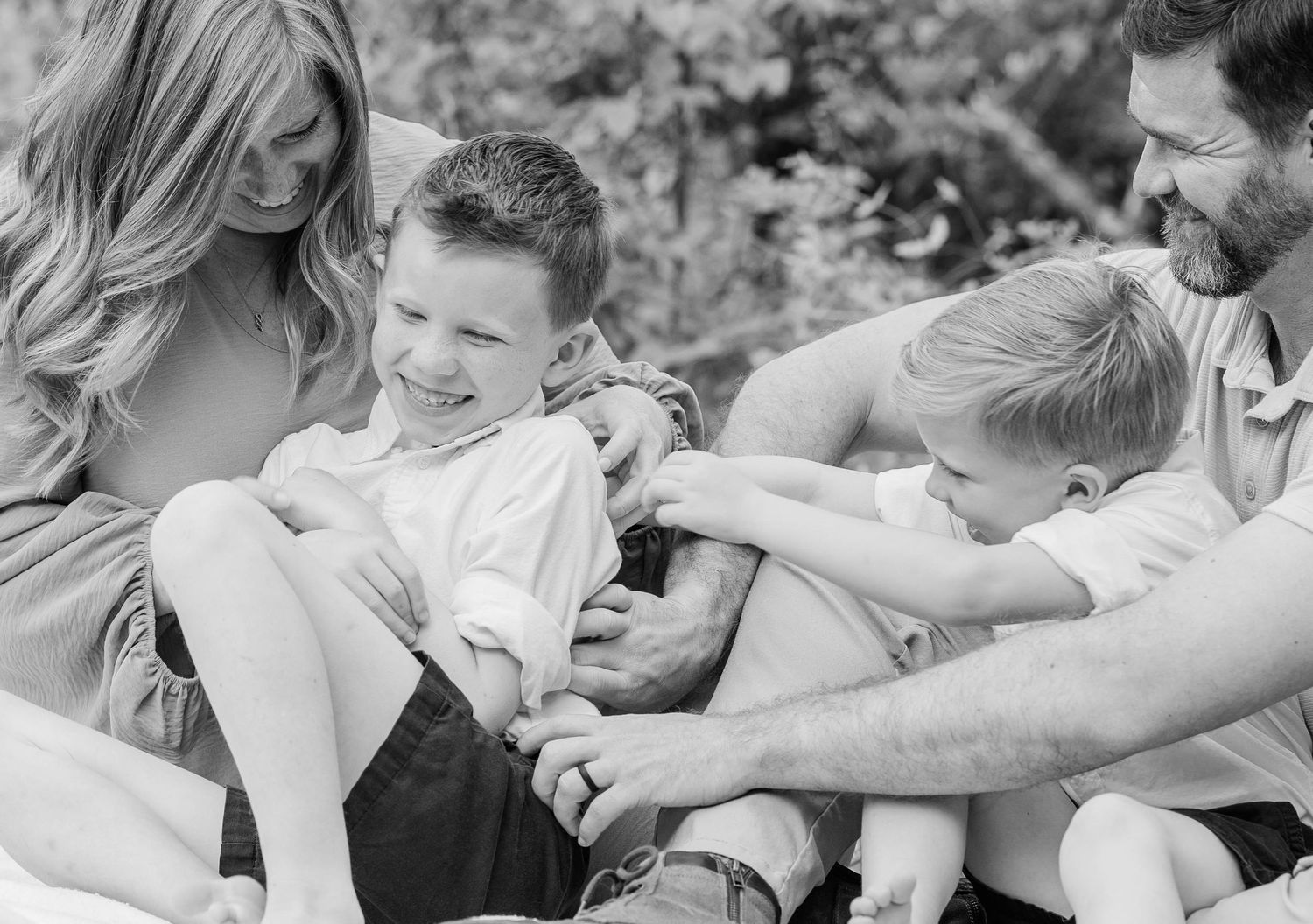 Black and white photo of family sharing playful moment outdoors on blanket.