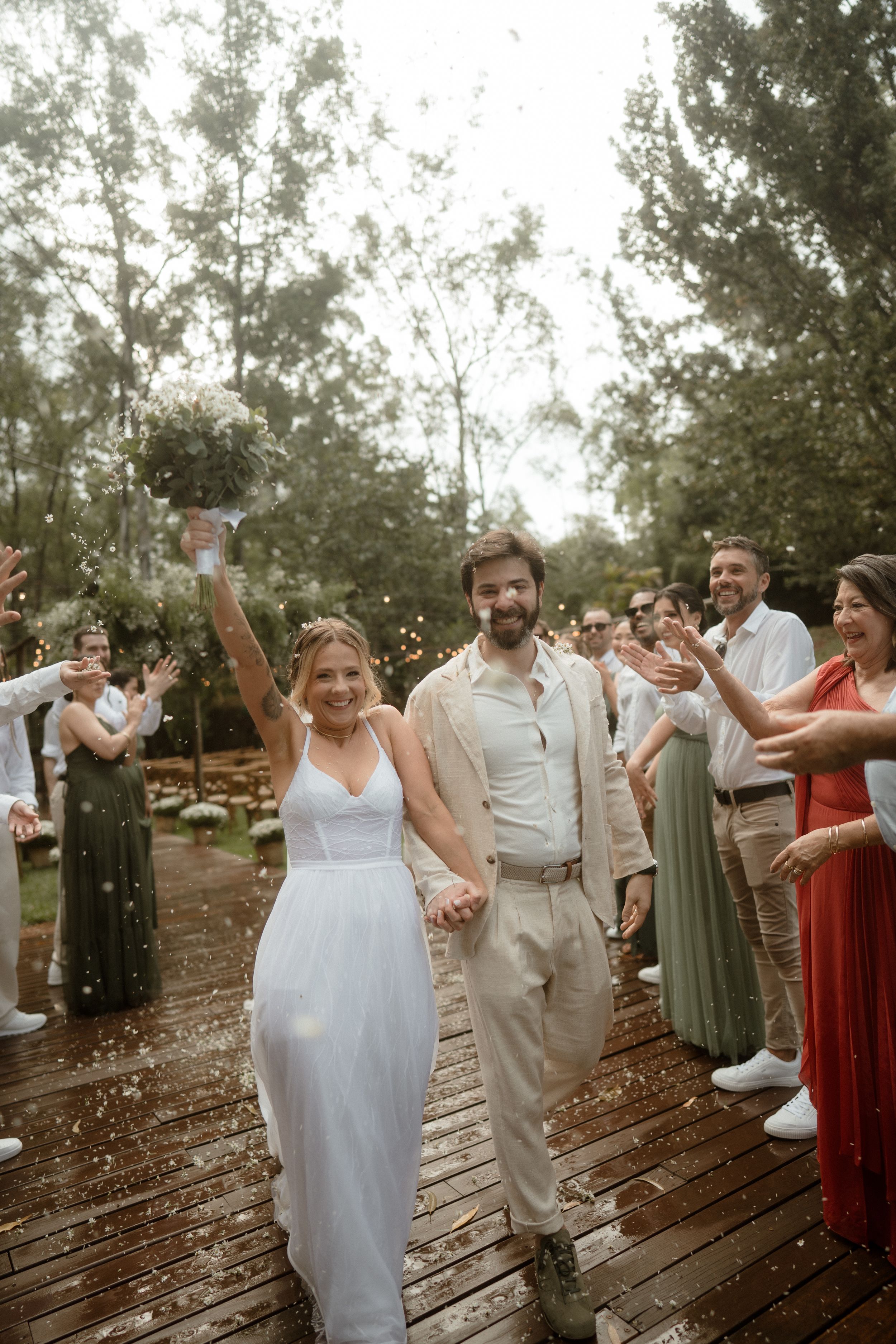 Wedding party celebrating on a wooden deck with guests in mixed formal attire.