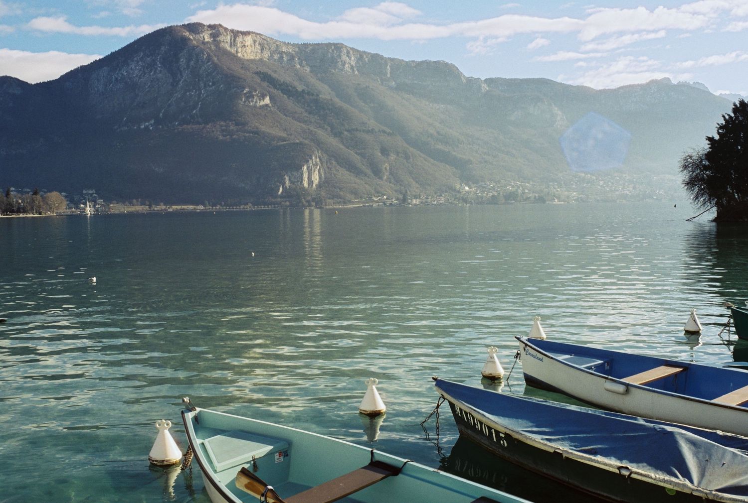 Boats moored on calm lake with majestic mountain backdrop on sunny day.