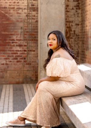 Elegant portrait featuring a sparkly champagne-colored formal gown against a rustic brick wall backdrop.
