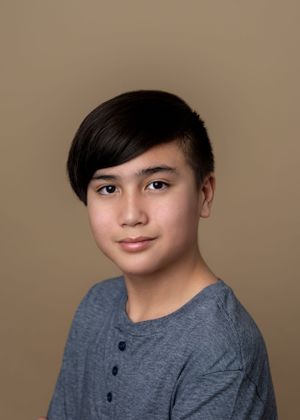 Professional studio portrait of young person in grey henley shirt against neutral background.