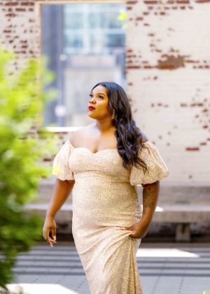 Glamorous portrait in a champagne-colored formal dress against weathered brick wall with greenery.