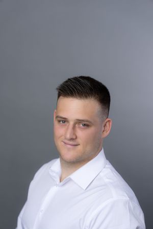 Professional headshot in white dress shirt against grey background with fade haircut.
