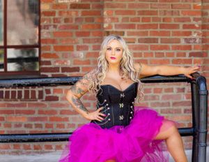 Woman in black corset and hot pink tulle skirt sitting on concrete steps.