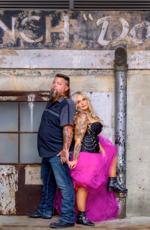 Couple poses dramatically against vintage wall with faded signage.