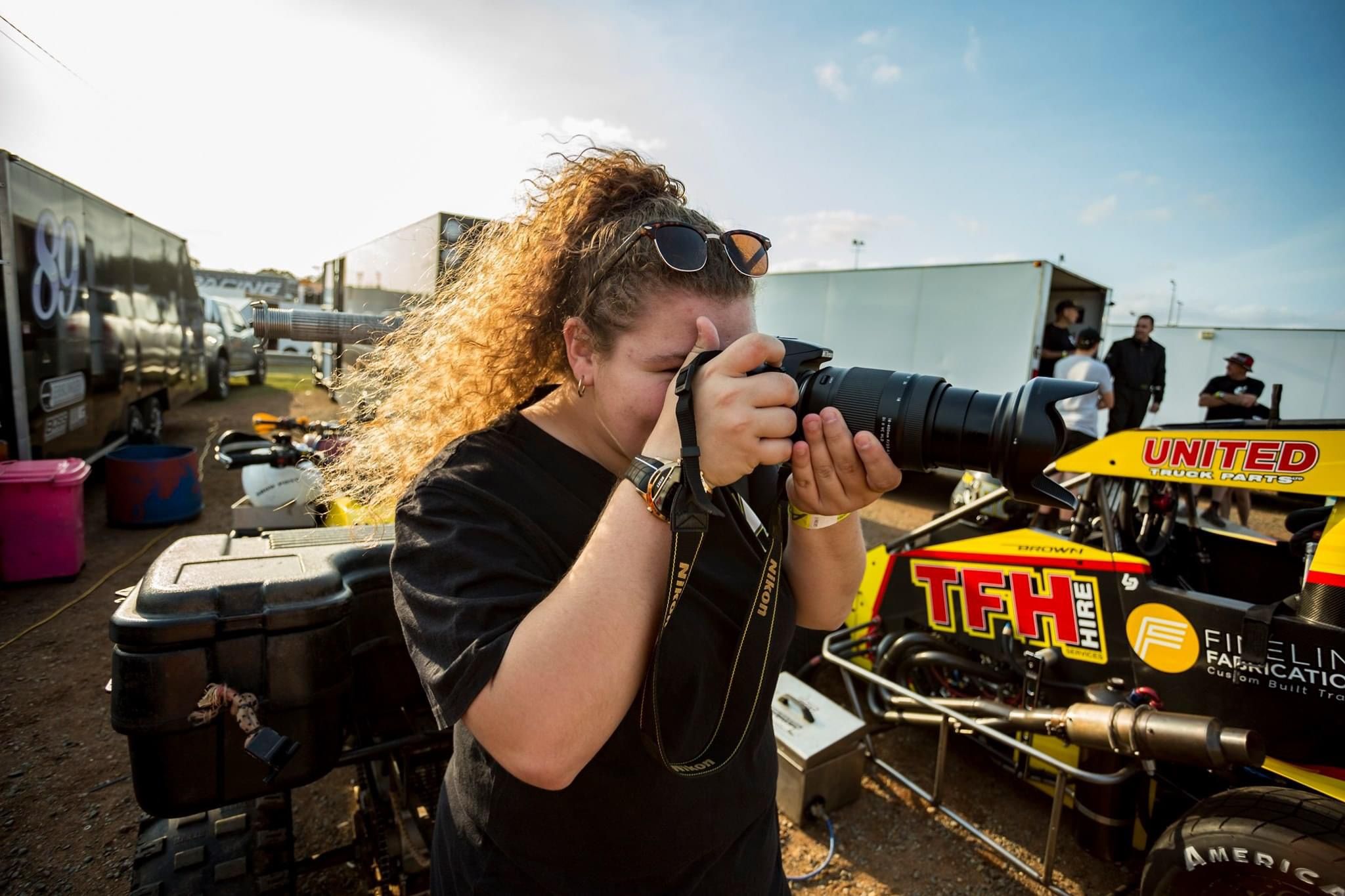 Photographer with curly hair using professional camera equipment outdoors.
