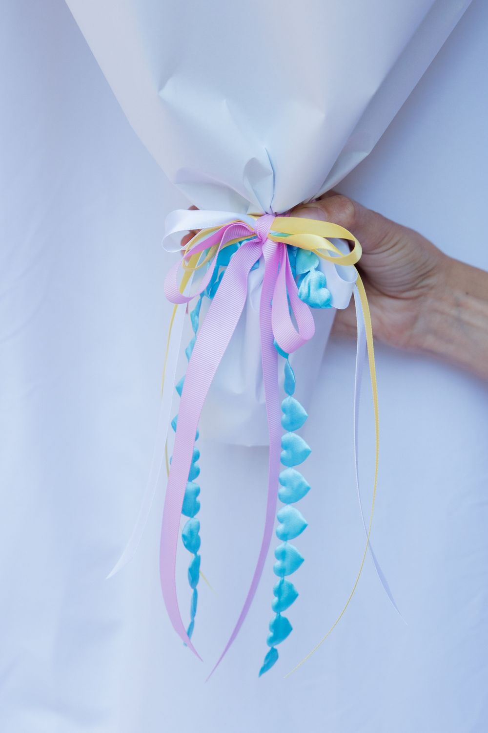Hand holding decorative ribbon bundle with pastel pink, yellow and blue curled streamers.