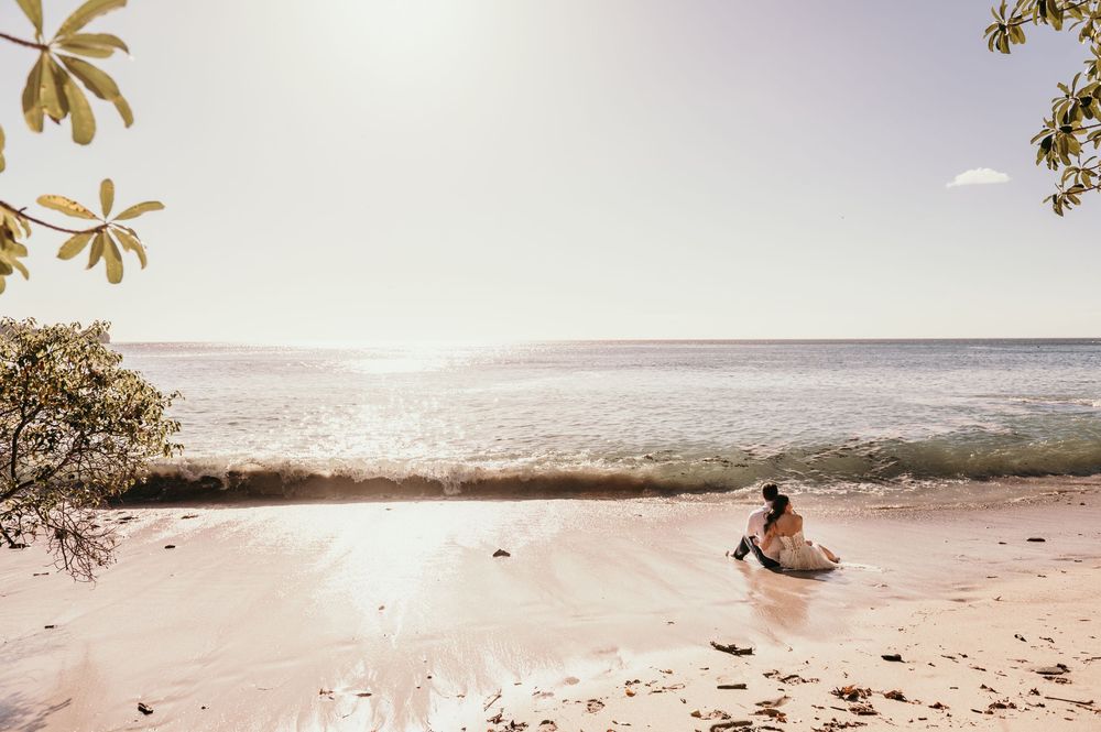 Someone sits peacefully on a serene tropical beach at sunset while overlooking the calm ocean horizon.