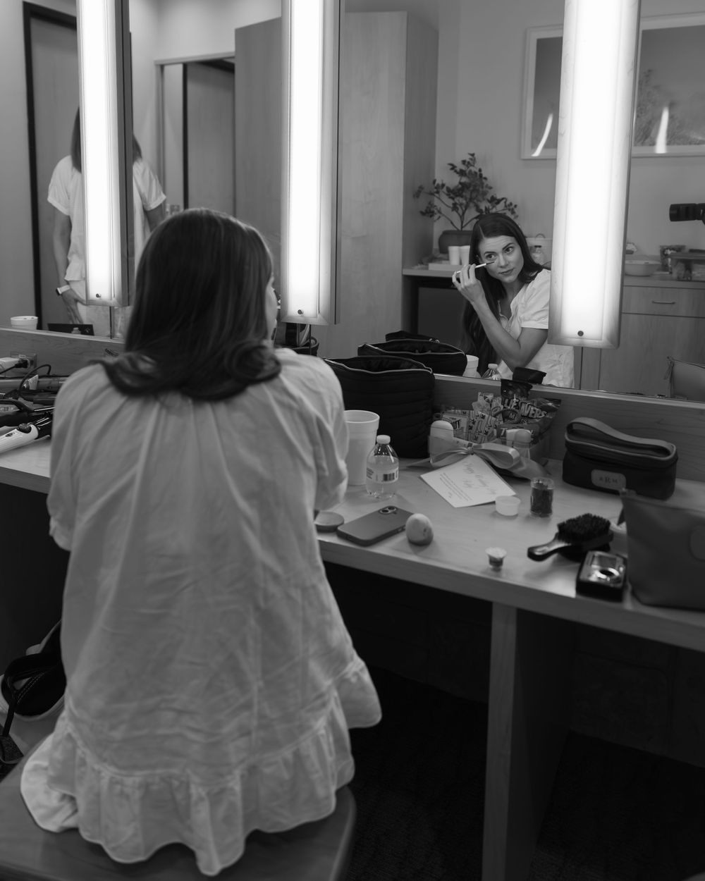A behind-the-scenes shot in a dressing room with bright vanity lights and mirror reflections.
