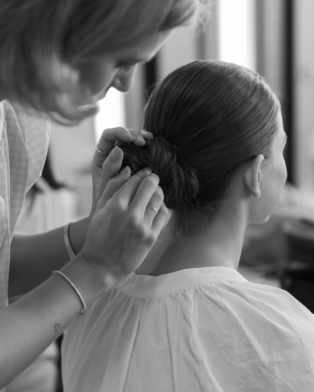 Hairstylist carefully styling and pinning up hair in an elegant updo during preparation, shot in black and white.