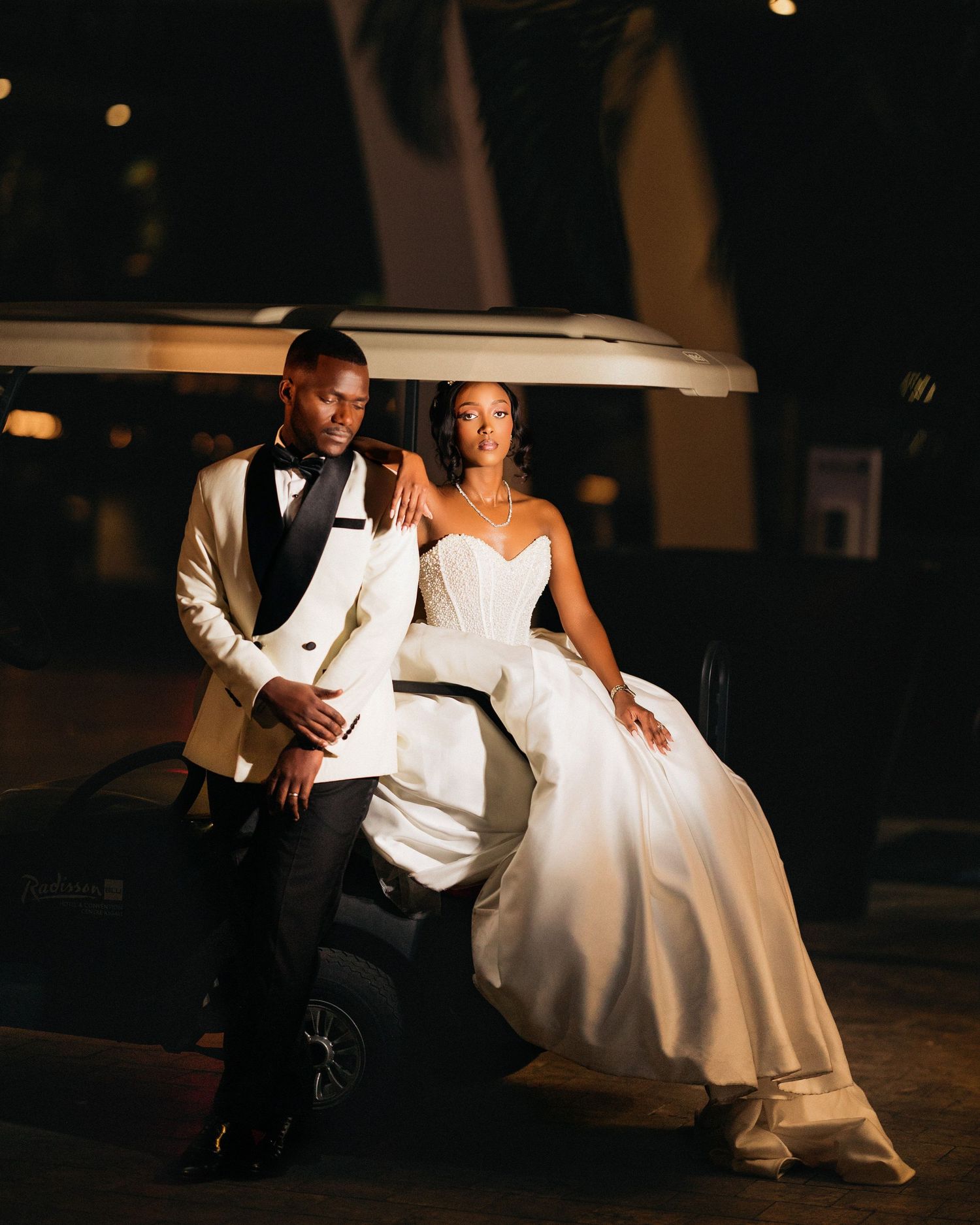 A bride and groom share an intimate moment on their wedding night, softly lit in a romantic evening setting.