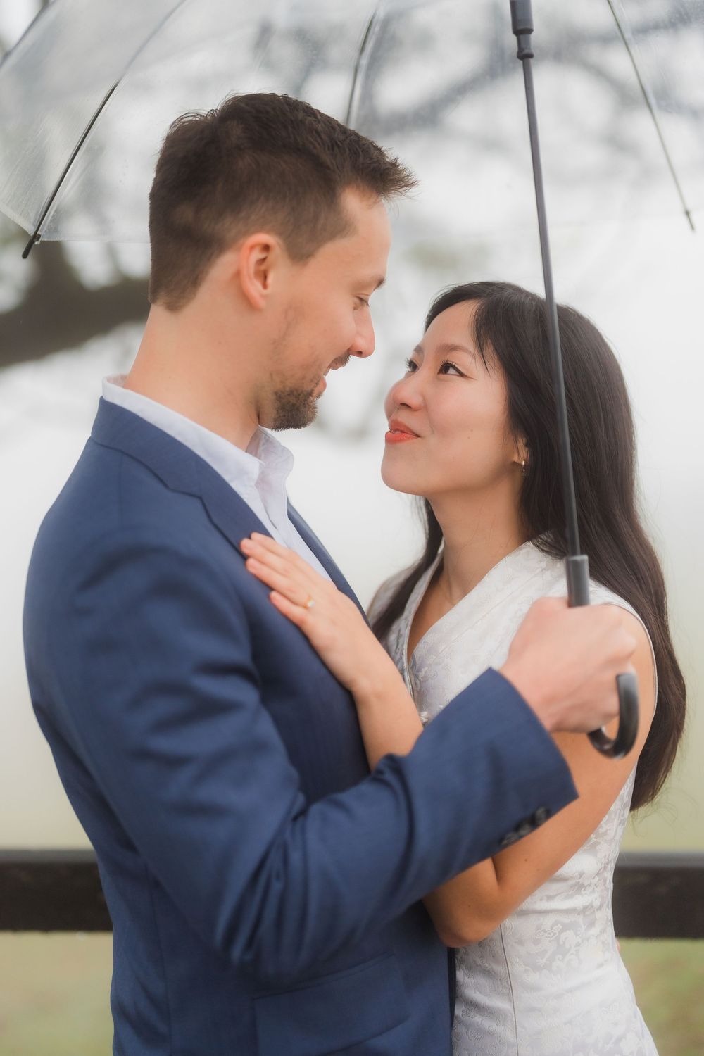 A romantic couple shares an intimate moment under a clear umbrella, the person in blue suit embracing their partner in white at Qingtiangang