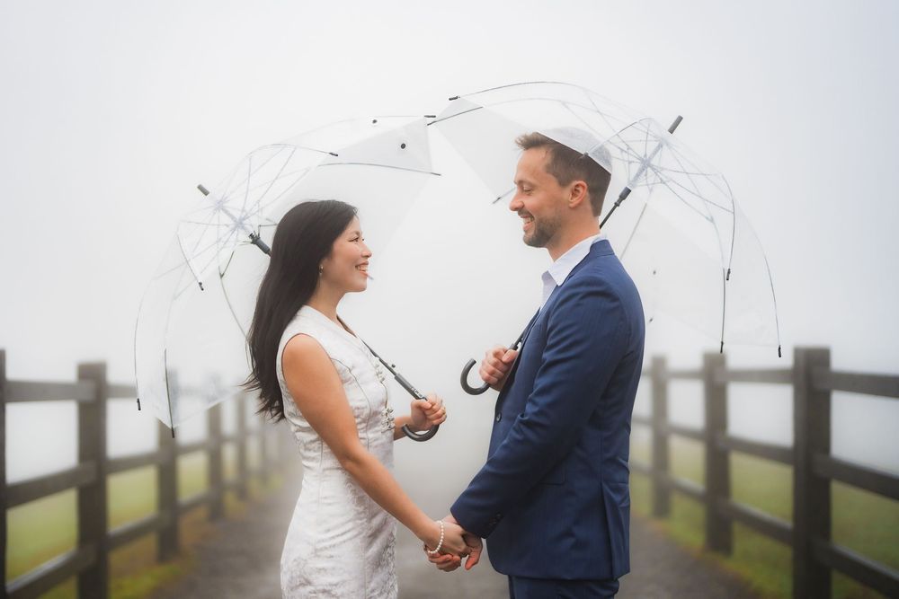 A couple shares a romantic moment under a clear umbrella on a misty wooden pier.