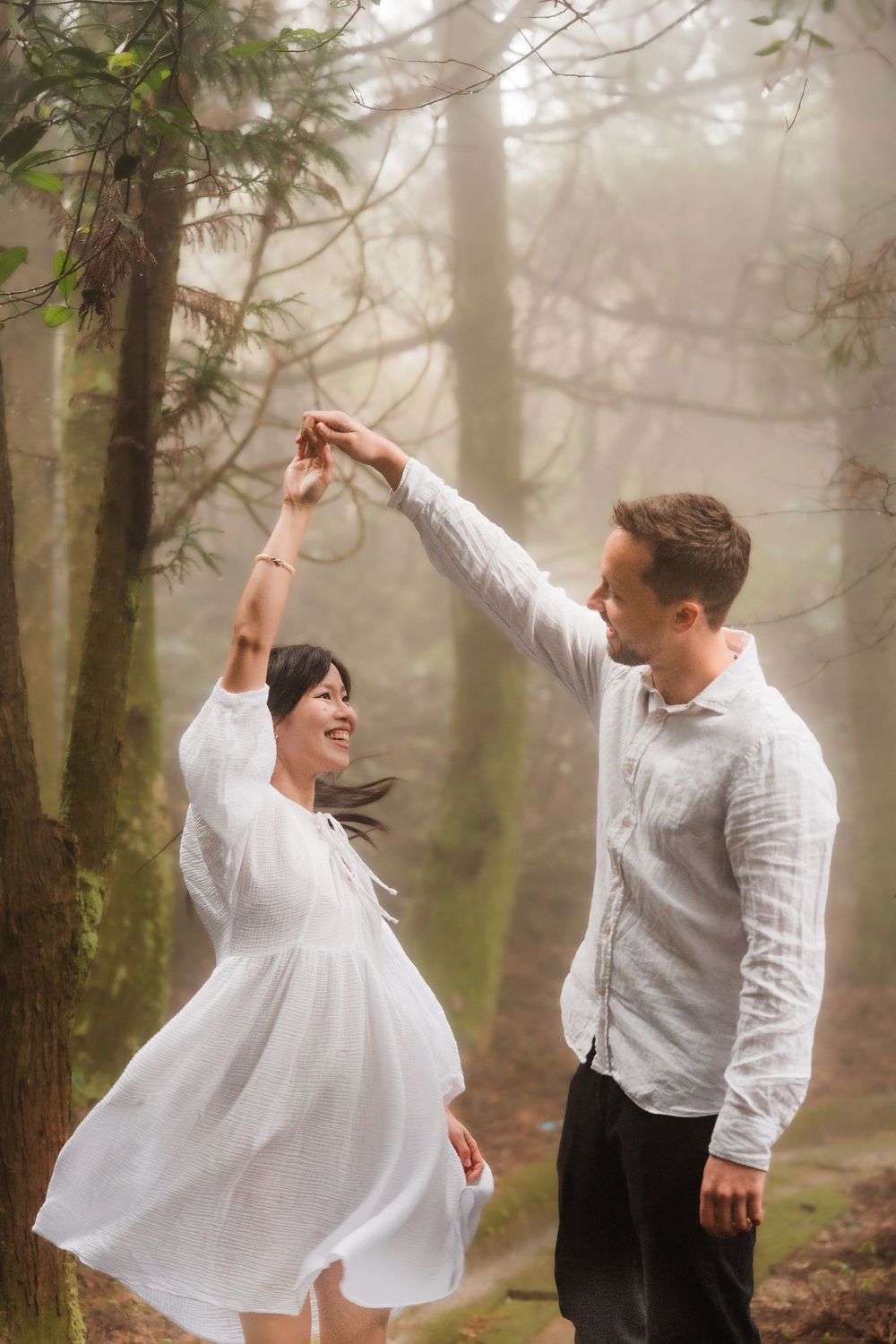 A couple in white clothing dance together on a misty forest path, creating a romantic and ethereal scene.