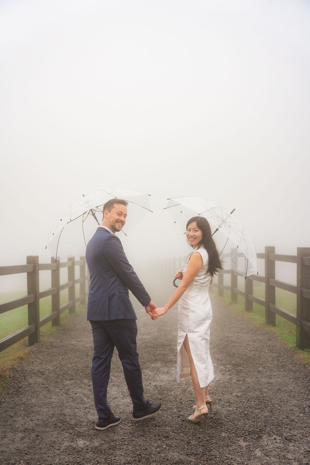A couple shares a romantic moment holding umbrellas on a misty path with wooden fencing in the background Qingtiangang in Yangmingshan Natio