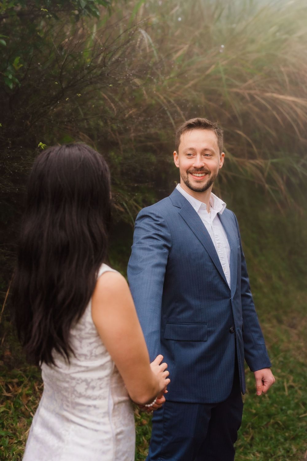 A couple shares a joyful moment outdoors, with one in a navy suit and one in a white dress against lush greenery at Qingtiangang.