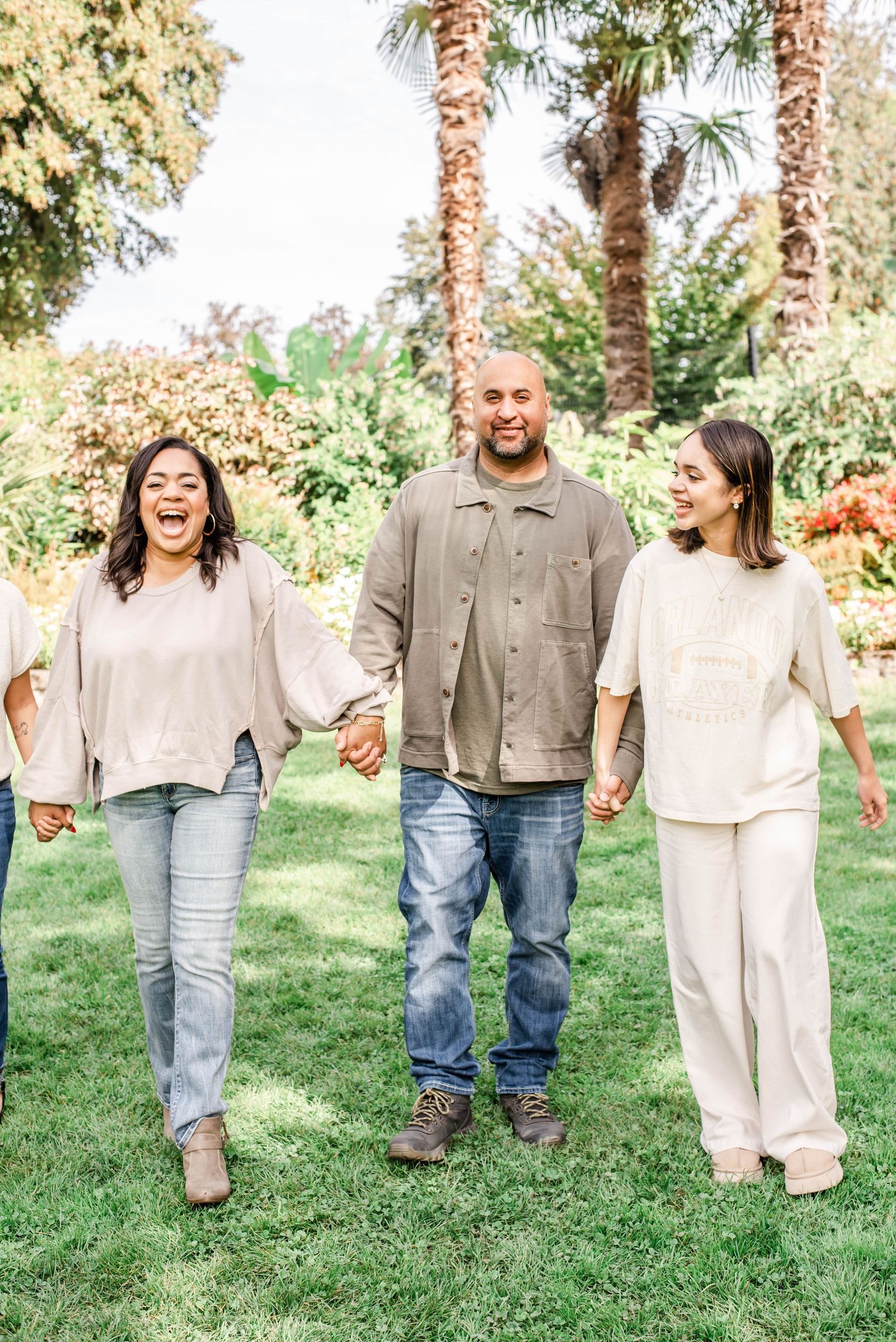 Family group holding hands while walking on green lawn with palm trees.