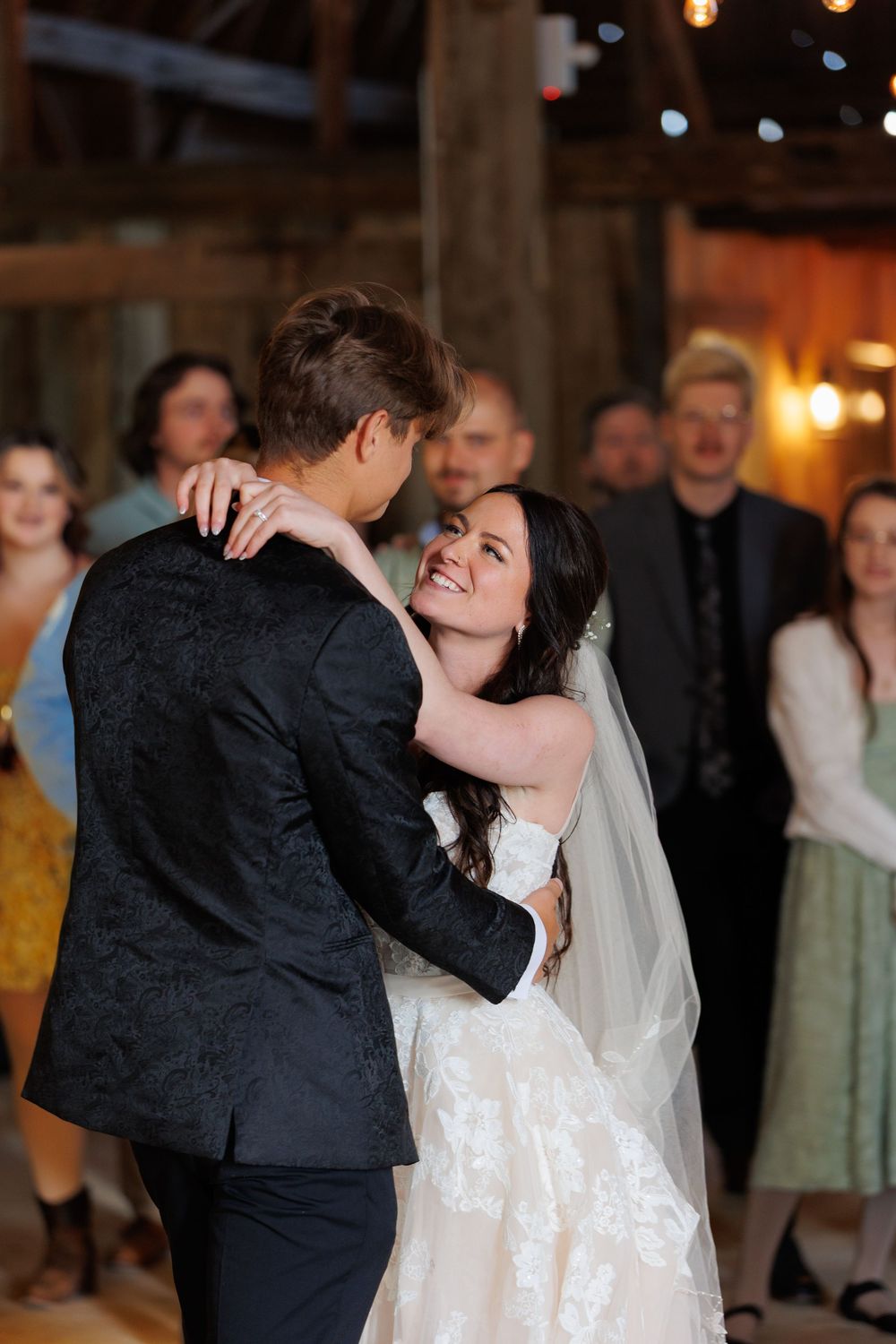 A couple shares their first dance at a rustic barn wedding reception with guests watching in the background.