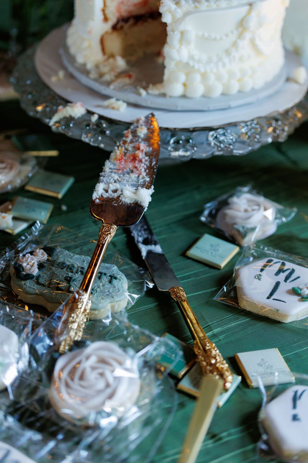 Wedding cake server and desserts displayed on a green tablecloth with decorative crystals and wrapped treats.