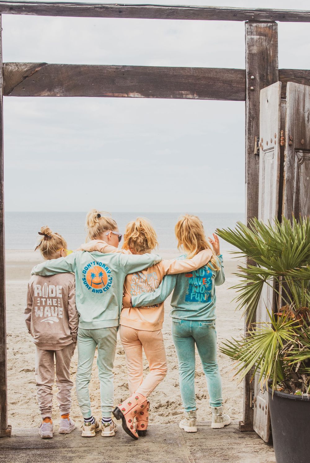 Four people wearing matching coastal-themed t-shirts stand together looking at ocean view from wooden deck.