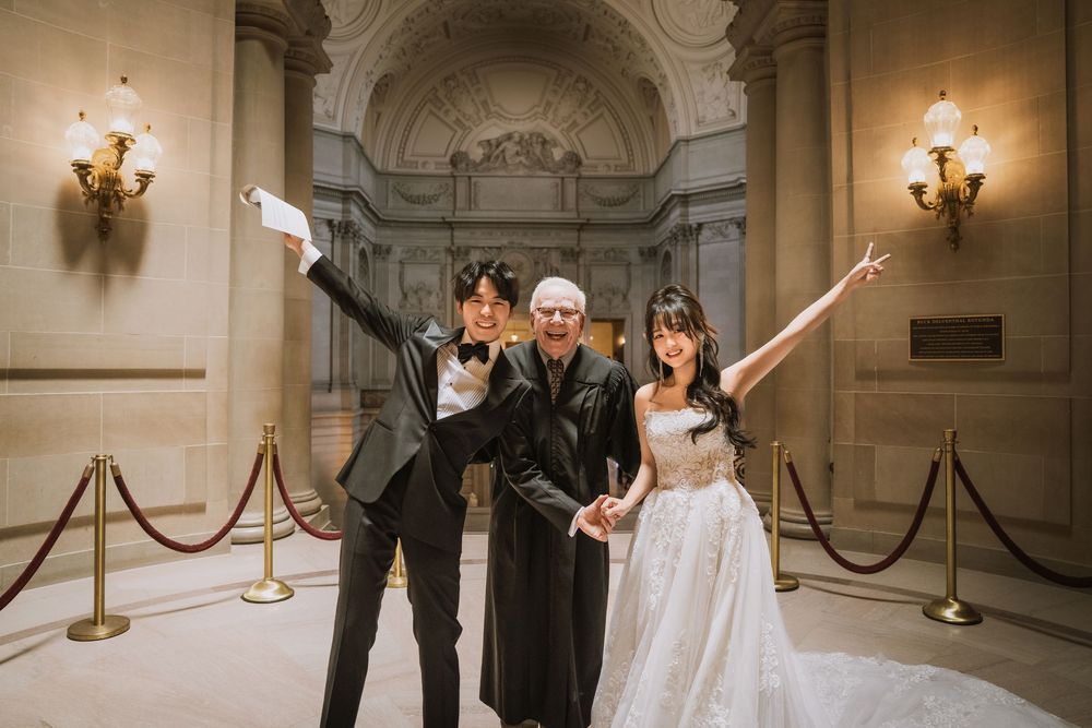 Wedding party poses in elegant hallway with rope barriers and ornate wall details.