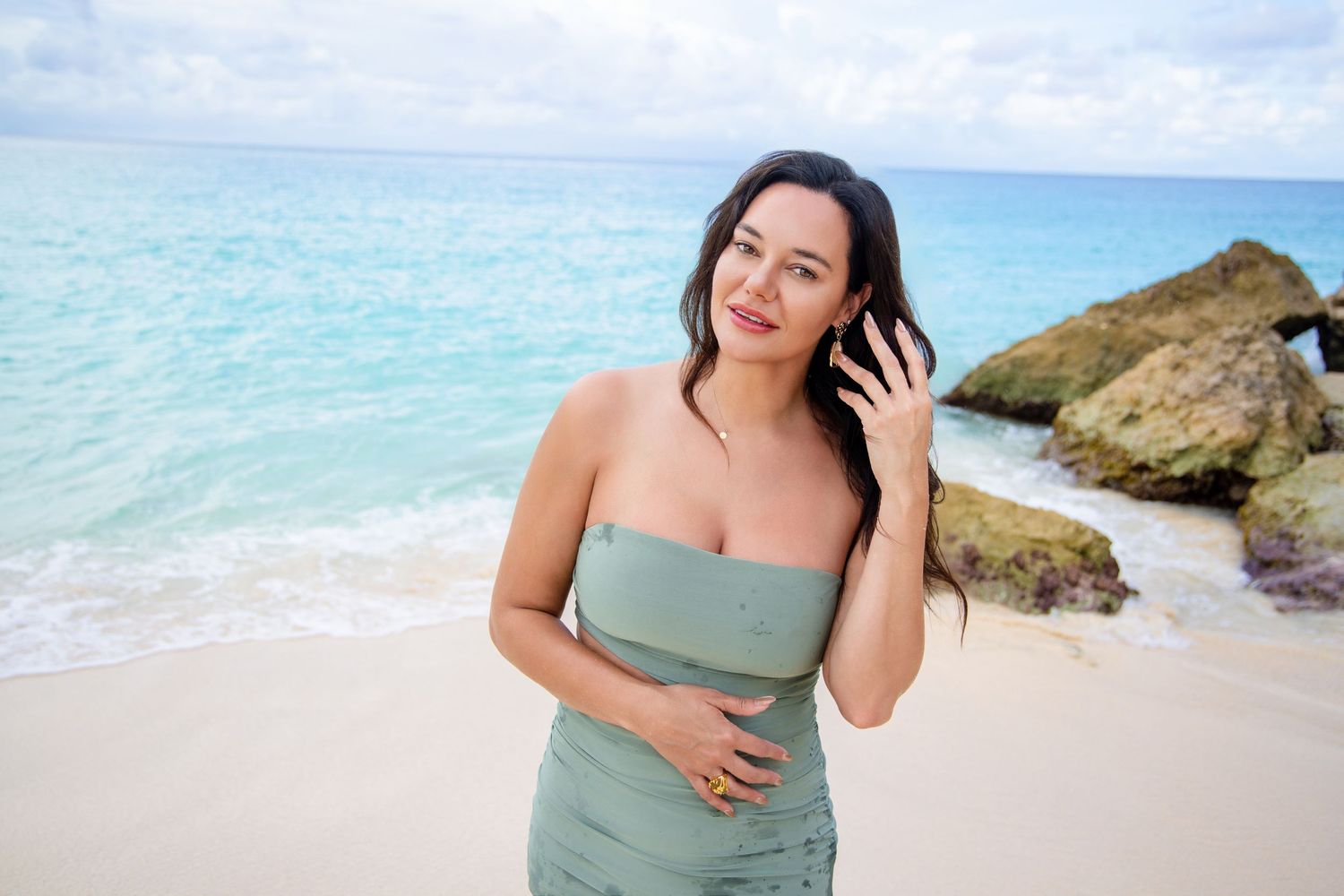 Woman poses confidently on Saint Maarten Beach with turquoise waves and rocky cliffs. Photo by Carolina Waldroff Photography