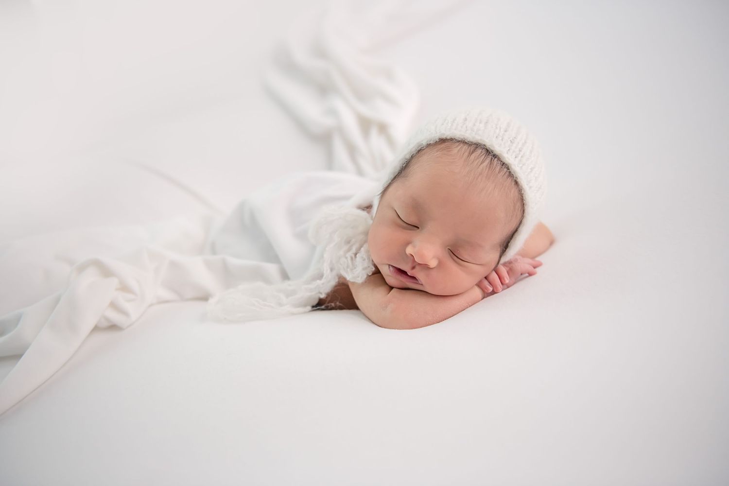 Peaceful newborn baby sleeping on white blanket with soft natural lighting.