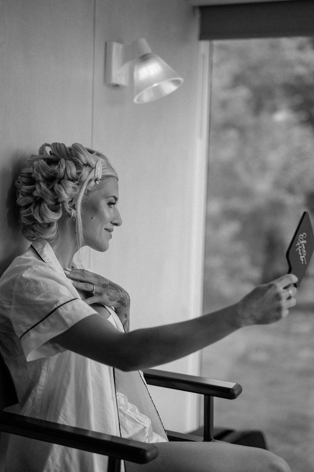 A person wearing hair curlers looks at their reflection in a mirror during wedding preparations.
