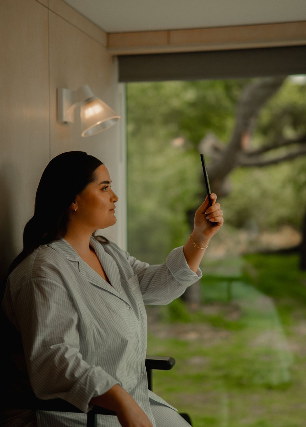 Person in gray robe looking at phone by window with soft natural lighting creating a peaceful atmosphere.