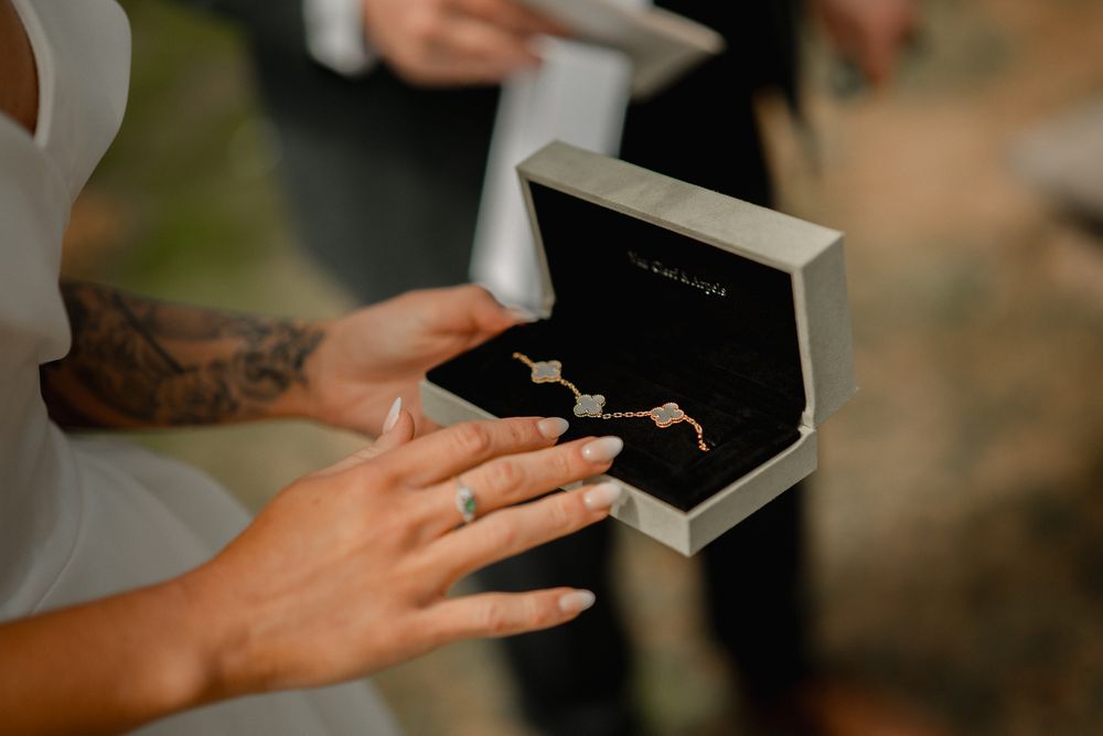 Close-up of hands with tattoos opening a small black box containing two wedding rings during proposal.