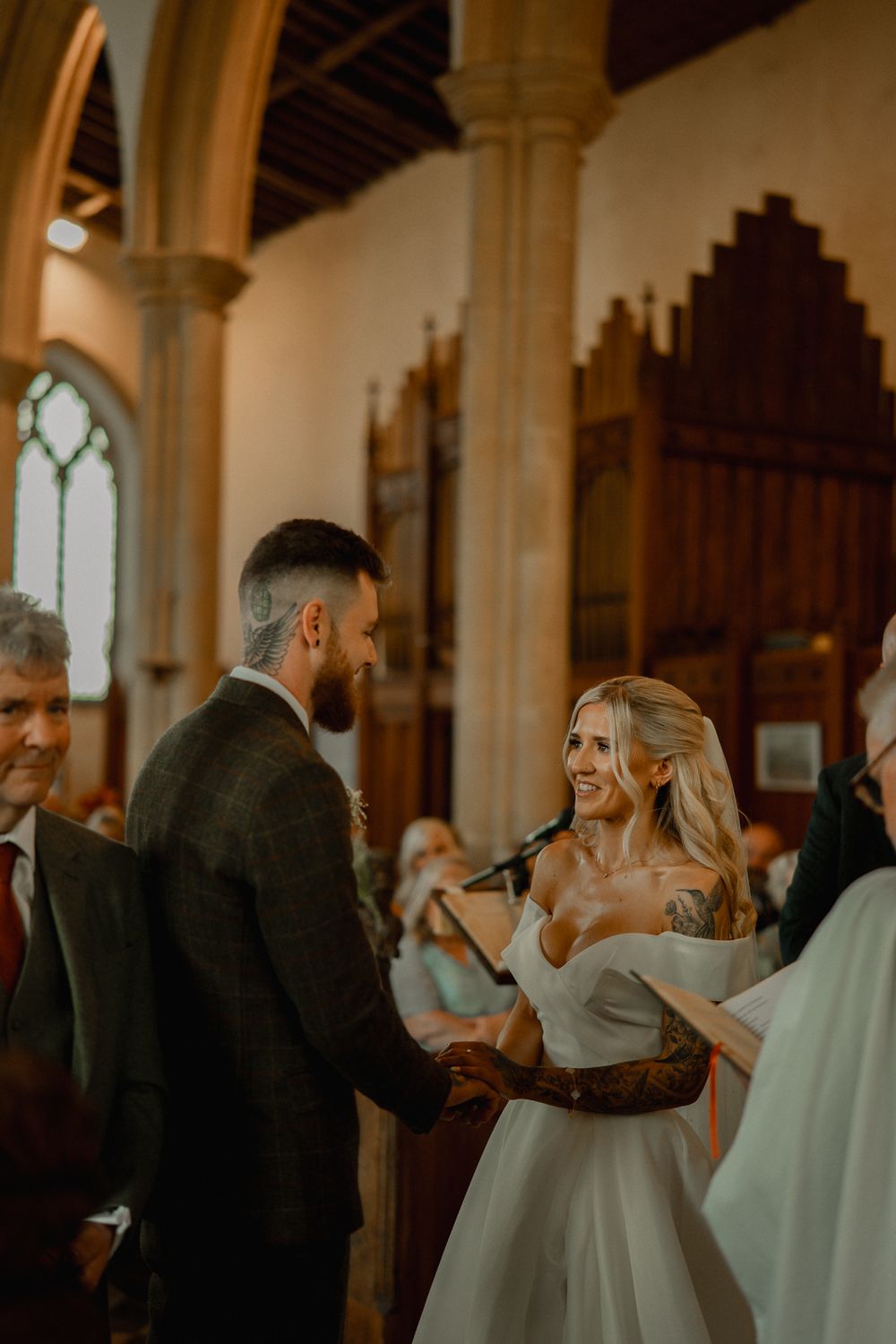 Couple exchanges vows during wedding ceremony in ornate church with gothic architecture and natural lighting.