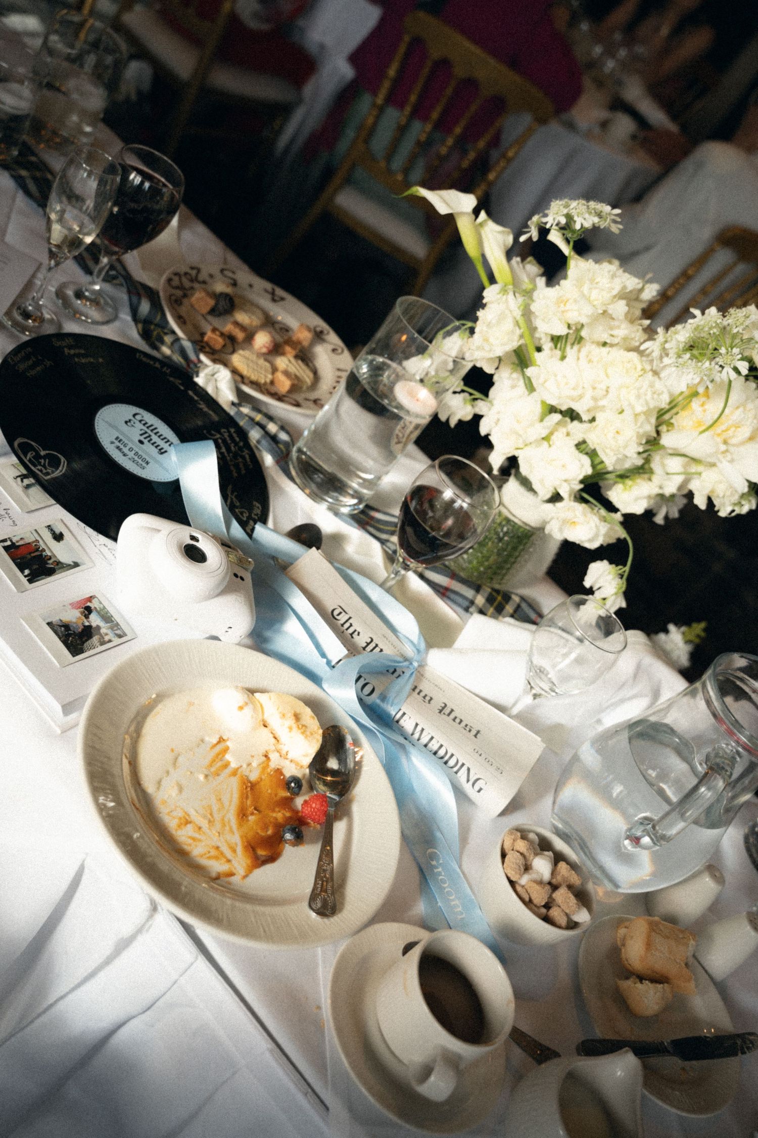 Elegant place setting at dining table with white hydrangea centerpiece, wine glass, and half-eaten meal on white tablecloth.