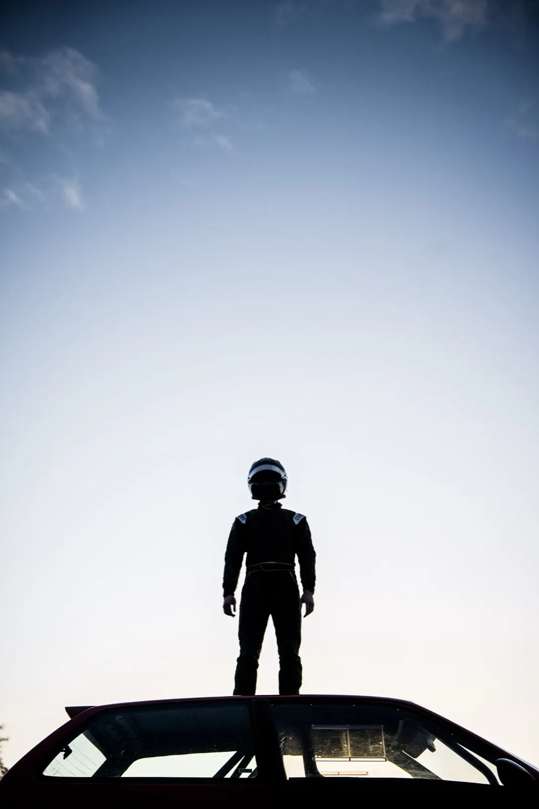 Silhouette d’un homme debout sur une voiture, en contre-jour sous le ciel.