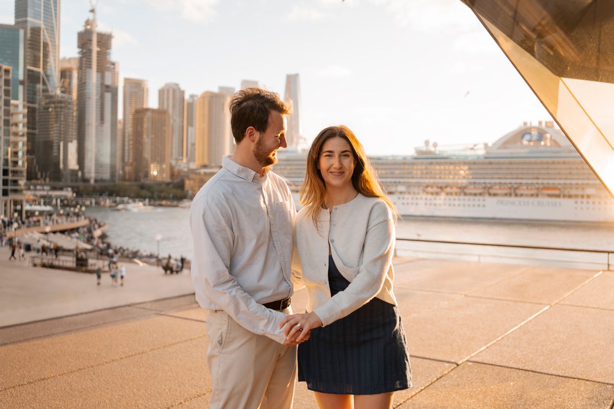 couple is happily smiling while having fun during their engagement photoshoot in Sydney at the Opera house with the yellow setting sun light