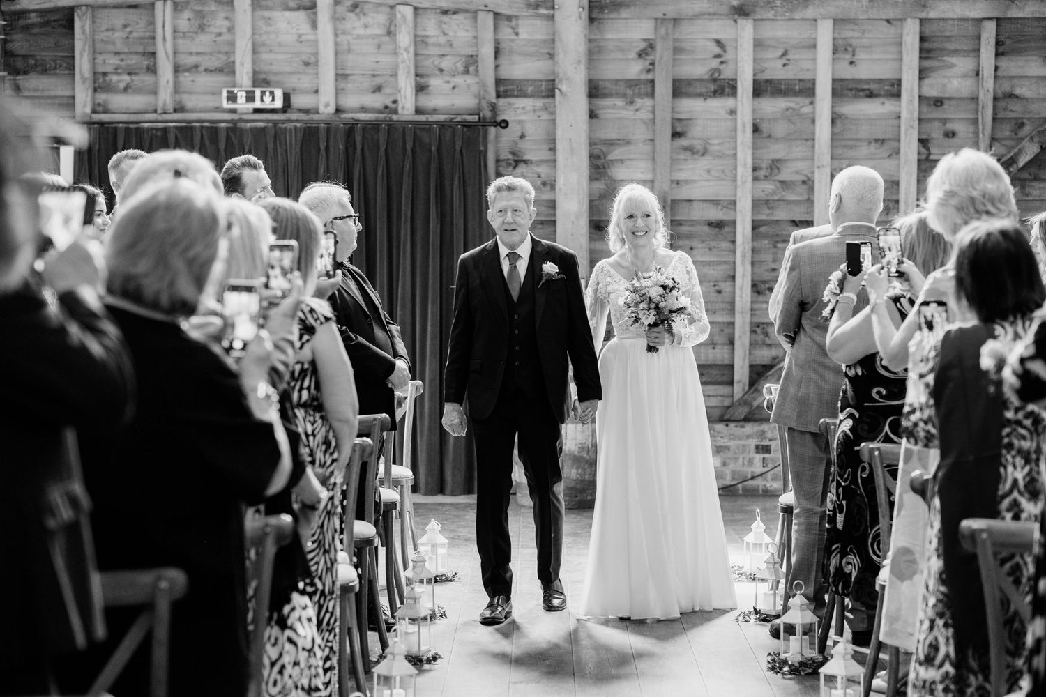 A black and white photograph of a wedding ceremony in a rustic indoor venue with exposed wooden beams.