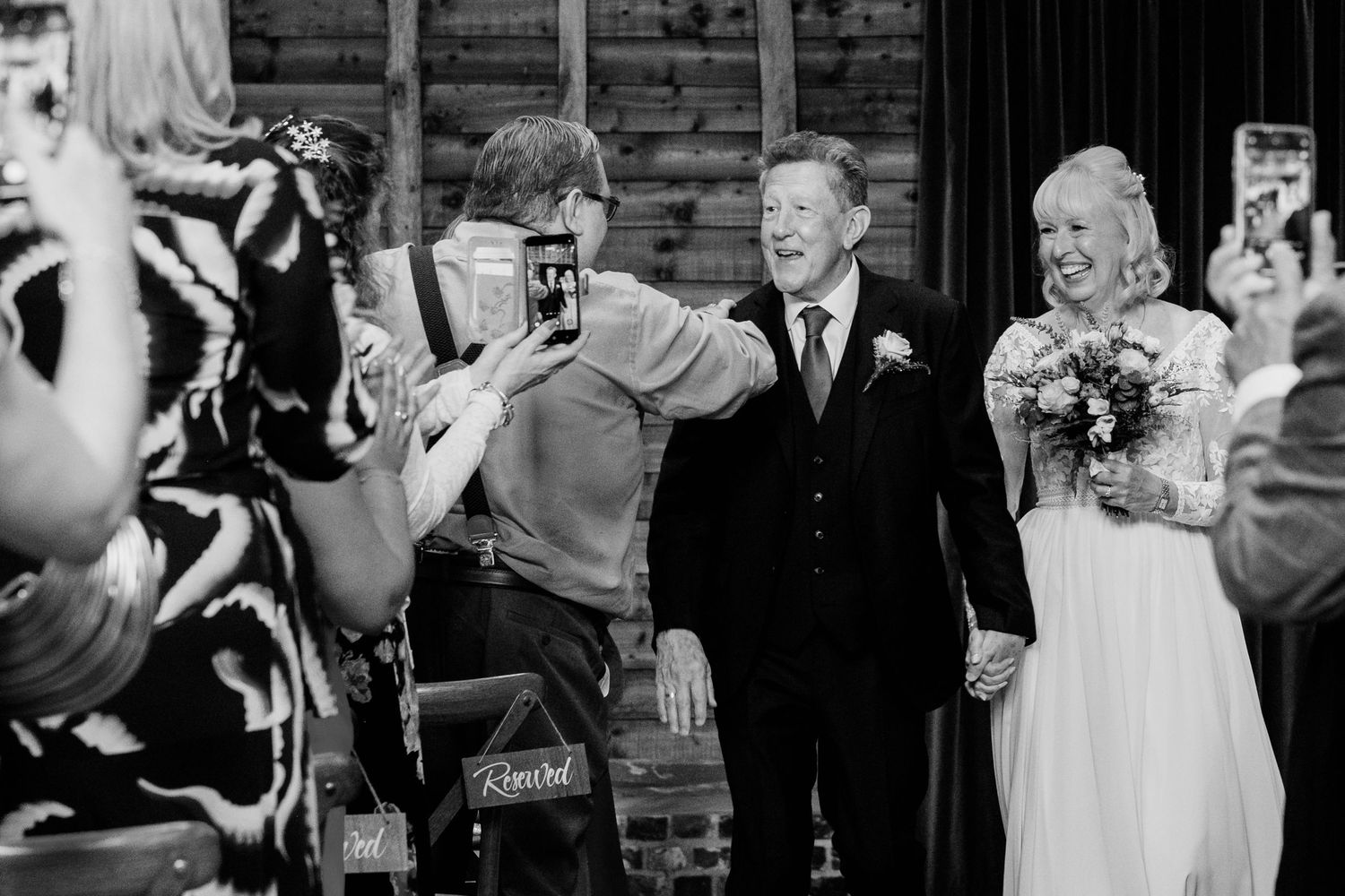 Black and white photo of wedding guests using cameras and phones to capture the newlyweds exiting their ceremony.