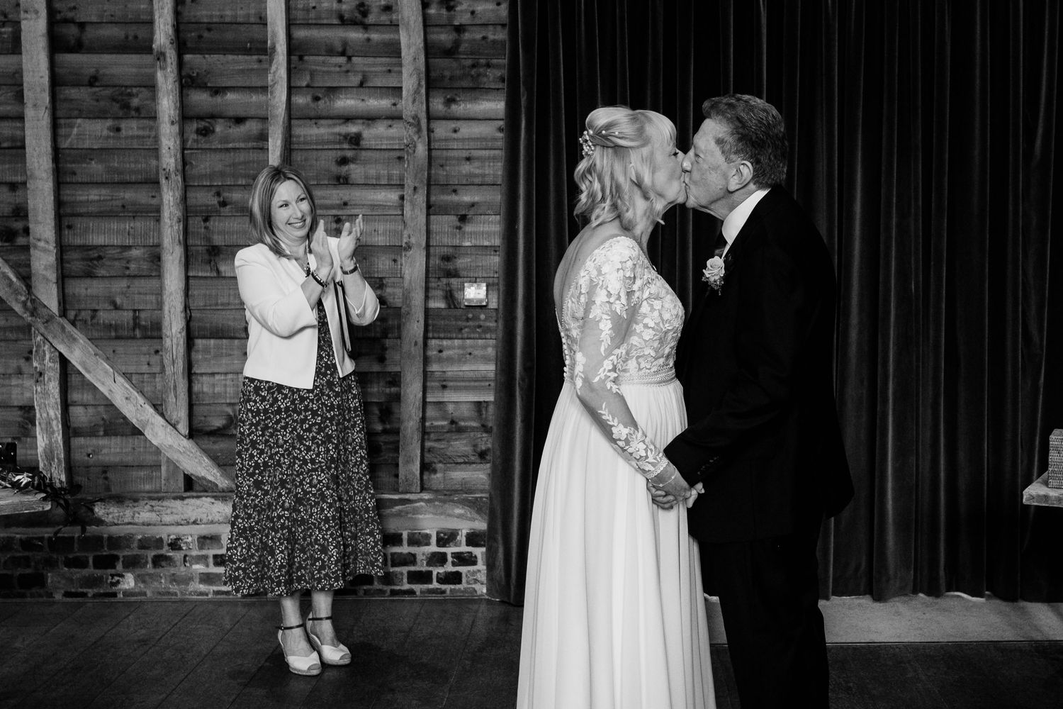 A wedding photographer captures a couple in formal attire against a rustic wood wall backdrop while celebrating their special day.