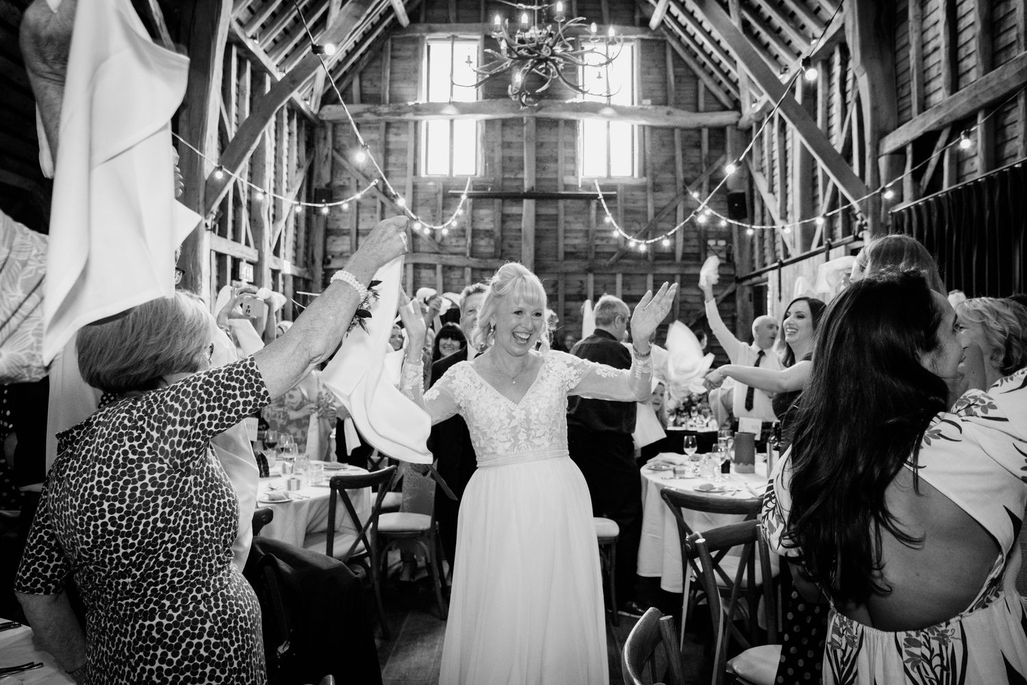 Black and white photo of people dancing and celebrating at a rustic wooden barn reception venue.