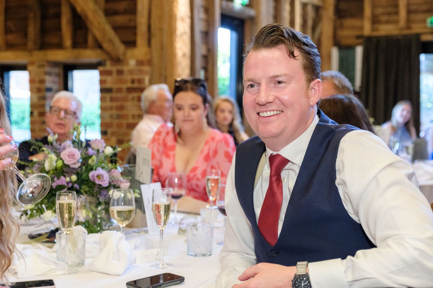 Guests enjoying a formal dinner reception at a rustic barn venue with elegant table settings and floral centerpieces.