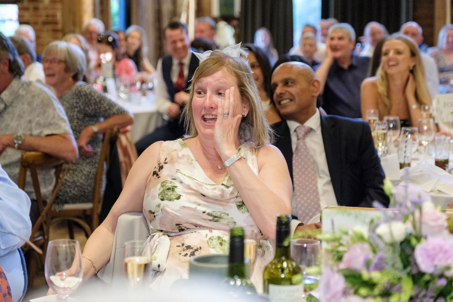 Guests enjoy a lively moment during an elegant wedding reception with floral centerpieces and formal table settings.
