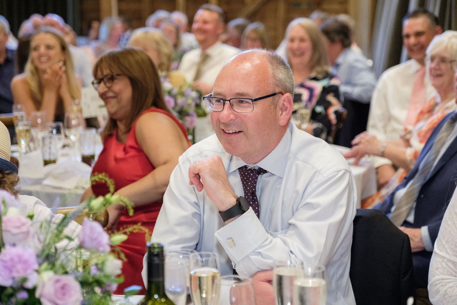 Wedding guests seated at decorated tables with floral centerpieces enjoy the reception celebration.
