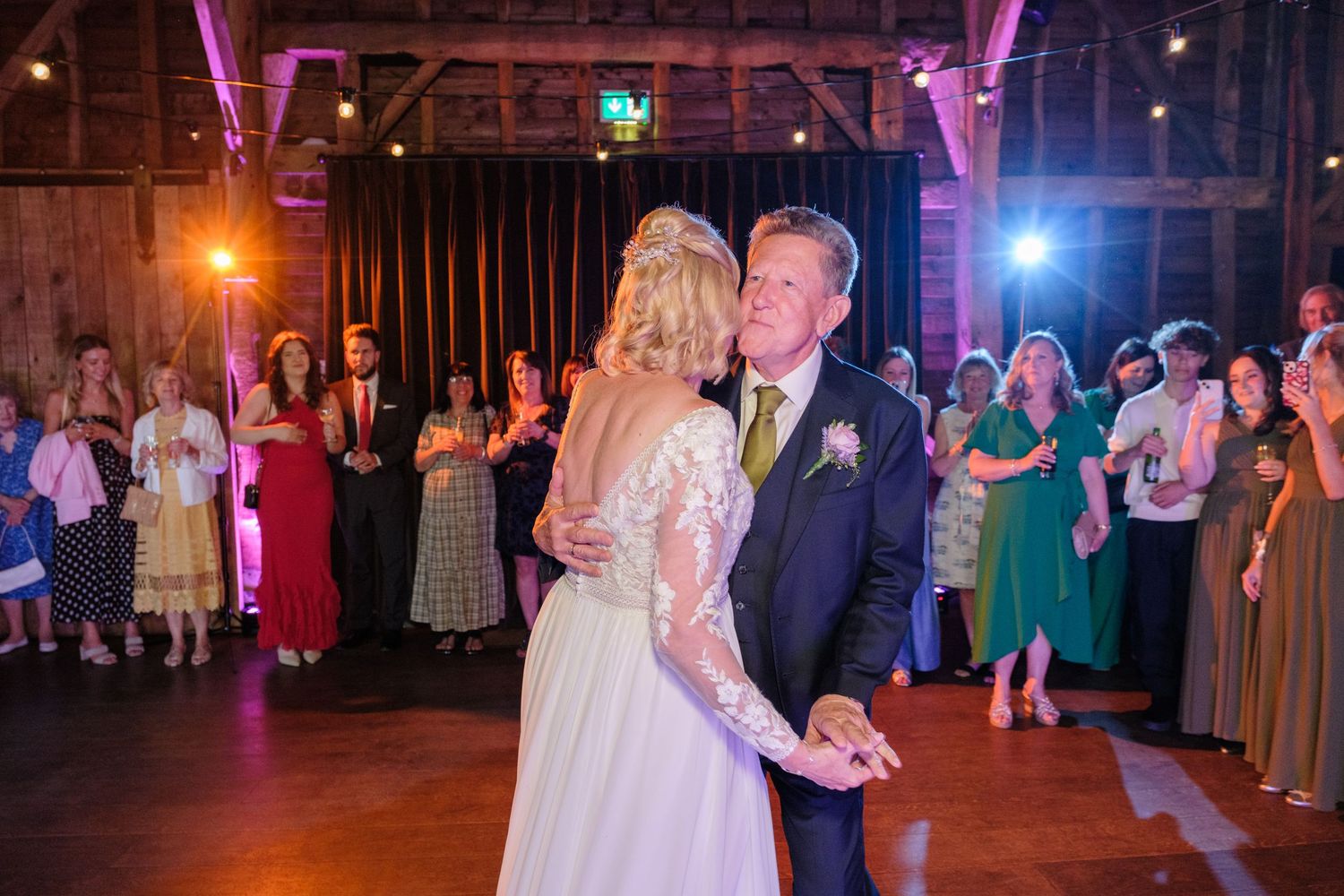 A couple shares their first dance at their wedding reception while guests watch from the dance floor with colorful lighting.