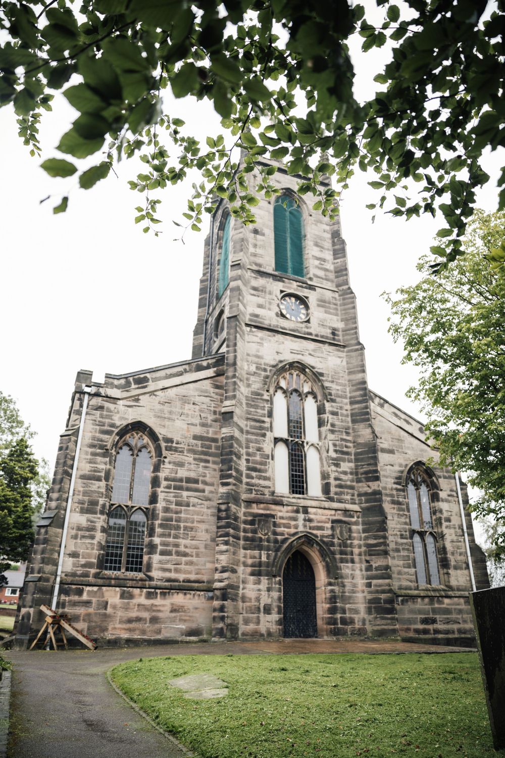 Historic stone church with Gothic architecture featuring pointed arches, tall steeple and green lawn in the foreground.
