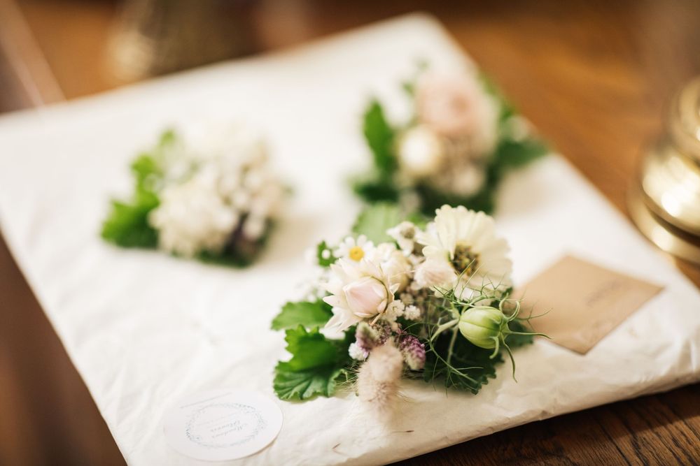 Elegant white floral boutonnieres with greenery on white linen.
