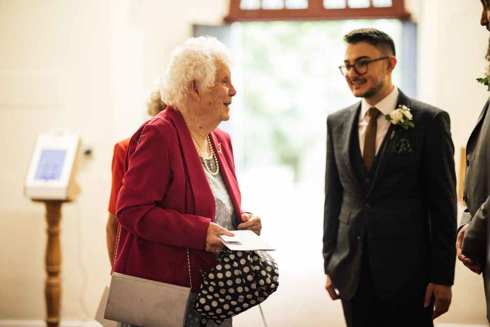 A guest in a red jacket engages in conversation during an indoor wedding reception.