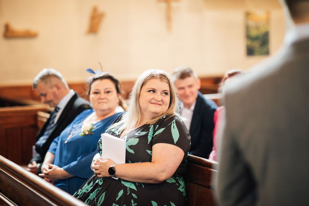 Wedding guests seated in wooden church pews during ceremony.